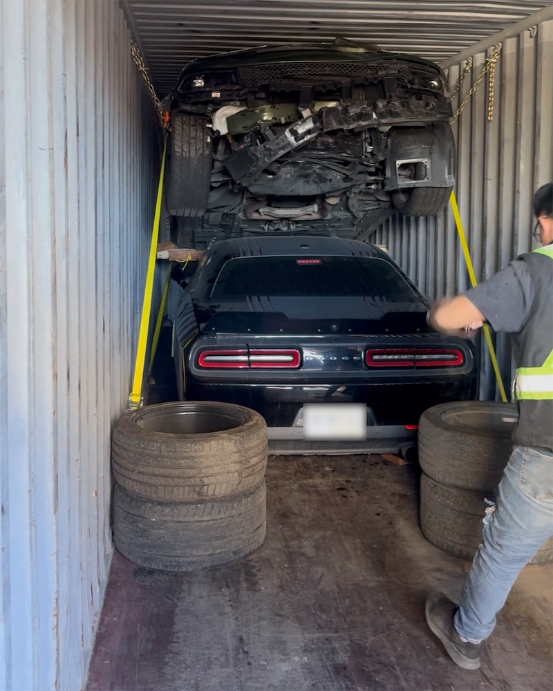 Worker strapping down two vehicles stacked inside a shipping container