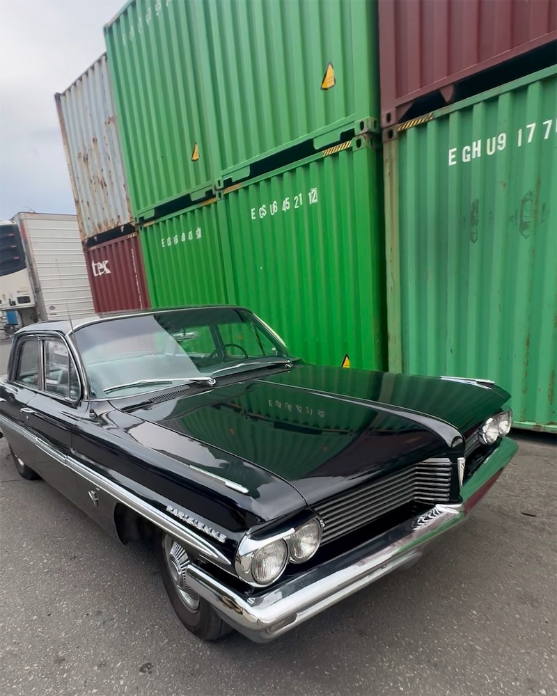 Classic black Pontiac Parisienne parked beside stacked shipping containers